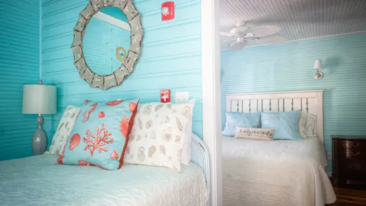 Two coastal-themed bedrooms with turquoise walls, white bedding, and seashell-patterned pillows in a Tybee Island vacation rental.