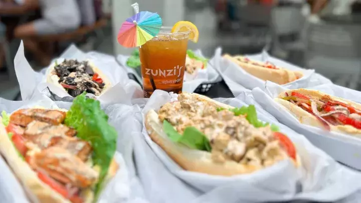 An outdoor table of sandwiches with a drink.