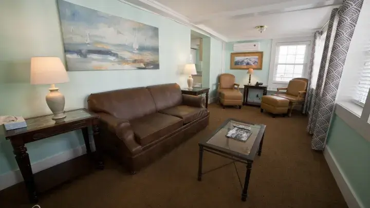 A living room with coastal blue painted walls, a couch, table, chairs, lamps and dark brown carpet.