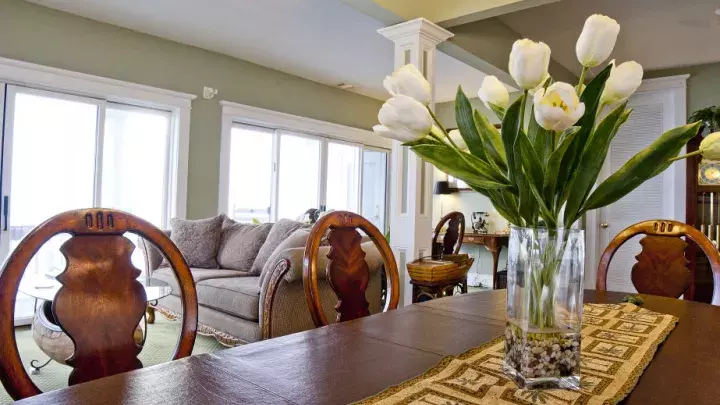 A dining table with a tulip centerpiece and view of a living room.