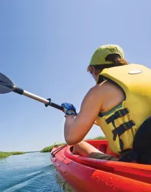 A person wearing a yellow life vest kayaking through a marsh.
