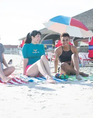 A girl’s group of three sitting and laughing on the beach on a sunny day.
