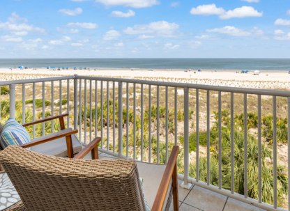Oceanfront balcony view on Tybee Island with wicker seating overlooking sand dunes, beach and calm shoreline.