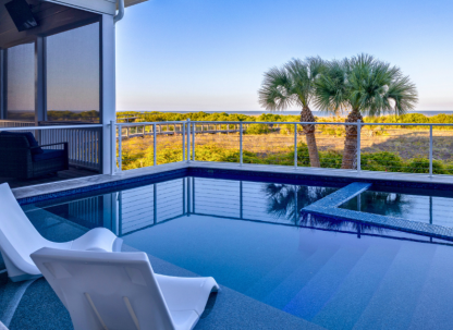Private pool with in-water lounge chairs overlooking coastal dunes and palm trees on Tybee Island, with a screened porch and elevated deck seating.