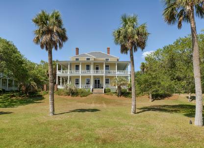Historic Officer’s Row home on Tybee Island featuring wraparound porches, tall palm trees, expansive lawn and classic coastal architecture on the North End.