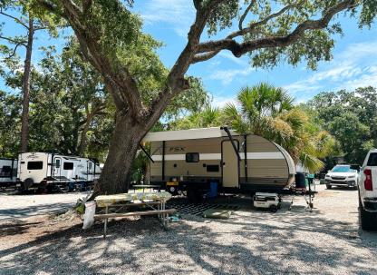 Travel trailer parked beneath a large shade tree at an RV site at River’s End Campground.